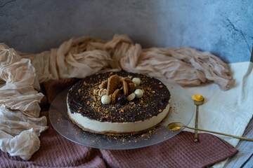 A luxurious Lotus Biscoff cheesecake topped with rich chocolate, beautifully displayed on a transparent plate. The dessert sits against a decorative background, enhanced by the elegance of gold spoons