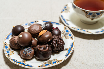 Assortment of fine filled chocolate bonbons on a plate with a cup of red tea.