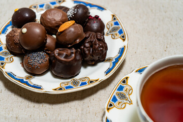 Assortment of fine filled chocolate bonbons on a plate with a cup of red tea.