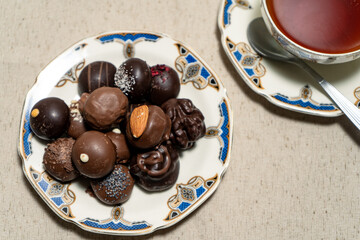 Assortment of fine filled chocolate bonbons on a plate with a cup of red tea.