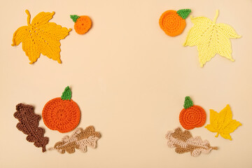 Autumn frame made of knitted toys in the shape of oak and maple leaves, orange pumpkins on beige background. Concept of autumn, Thanksgiving, Halloween