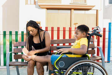 Dark-skinned brothers are sitting in a park. The African girl with braids checks the foot of her...