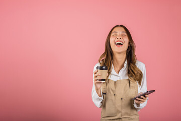 Portrait Asian happy young woman barista bar tender coffee maker holding coffee tea hot cup and mobile phone studio shot isolated on pink background, female smiling hold takeaways cup and smartphone