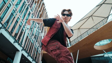 Low angle of asian attractive hipster pose at camera surround by mall. Portrait of break dance choreographer looking at camera while dancing in hip hop style. Outdoor sport 2024. Hiphop.