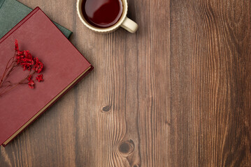 Books with flower and cup of tea on wooden background from above. Flat lay, top view.