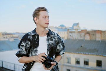 Caucasian man holding camera against urban rooftop background under clear sky, capturing details of...