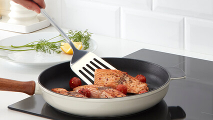 Closeup of a person flipping salmon fillets in a frying pan.