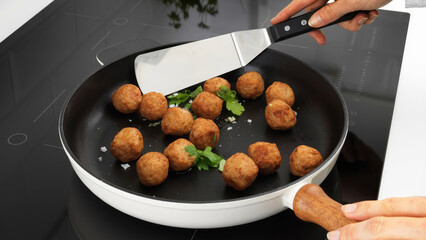 Closeup of a person flipping meatballs in a frying pan.