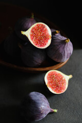 Close up of fresh ripe fig fruits in a wooden bowl on dark grey table 