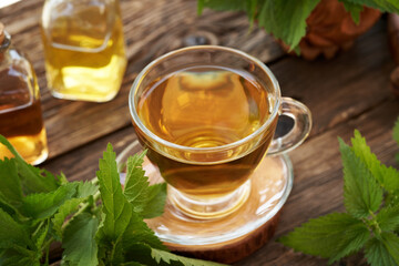 A cup of herbal tea with fresh nettle leaves on a table