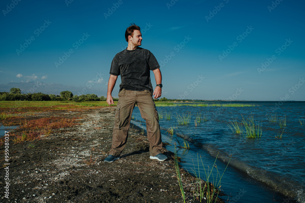 Poster young handsome man standing on lake shore on summer day