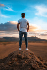 Fototapeta premium A man stands on top of a small hill, looking out over a wide, open landscape as the sun sets in the distance.