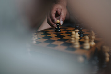 A close-up of a person's hand strategically moving a chess piece on a classic wooden chessboard,...