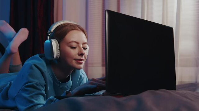 A stunning white woman with red hair relaxes on a bed by the window, bathed in the gentle glow of evening light, while she looks at her phone, possibly working or studying