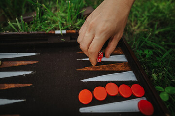 Hand placing dice on a backgammon board set on grass. Outdoor leisure activity showcasing...