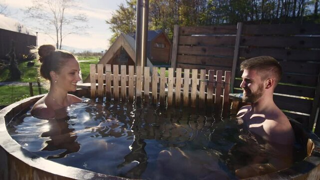Young couple enjoying in outdoor hot tub, soaking in warm water, surrounded by the pristine nature, close up shot. Glamping and relaxation concept.