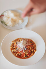 Scattering freshly grated parmesan over the pasta. Spaghetti with tomato sauce and basil on a plate. Hands grating Parmesan cheese on a spaghetti pasta. Traditional Italian food. 