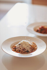 Scattering freshly grated parmesan over the pasta. Spaghetti with tomato sauce and basil on a plate. Hands grating Parmesan cheese on a spaghetti pasta. Traditional Italian food. 