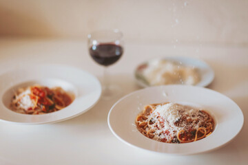 Scattering freshly grated parmesan over the pasta. Spaghetti with tomato sauce and basil on a plate. Hands grating Parmesan cheese on a spaghetti pasta. Traditional Italian food. 