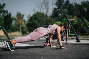Woman engaging in a calisthenics workout in a park, performing push-ups on a sunny day. Outdoor fitness and exercise concept.