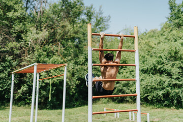 Fit strong male sports person working out on an outdoor pull-up bar in the park, showcasing...