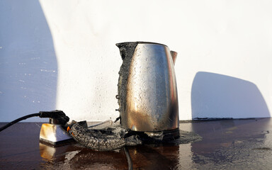 Burning Electric kettle. Electric kettle for tea caught on fire over table. Electric kettle melted due to a short circuit in electrical wiring. Overloaded electrical current or short in device