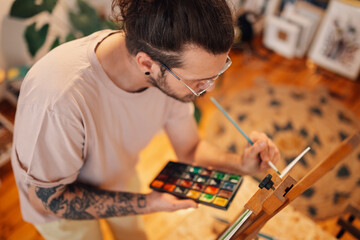 Top view of artistic hipster painting at atelier with watercolor on easel