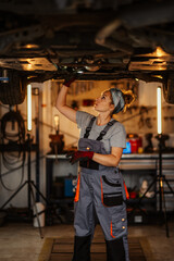 Professional female mechanic examining under lifted car at mechanic shop