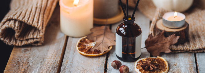 Concept of cozy fall home atmosphere, aromatherapy. Perfume, apartment aroma diffuser with autumn scent of pumpkin spicy sweet pie, cinnamon, anise. Room decor: pumpkins, dry orange, wool plaid banner