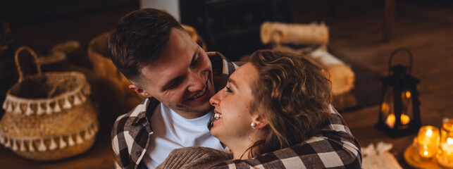 Beautiful young loving couple relaxing near fireplace in bed at home. Happy spouses enjoying lazy romantic winter cozy morning in bedroom. Candles, garlands, countryside interior. Romantic date banner