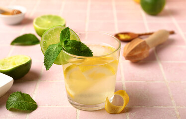 Glass of infused water with lemon on pink tile background