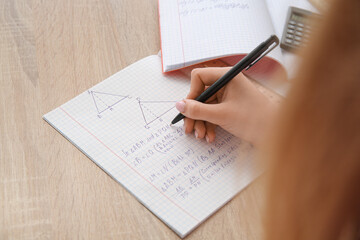 Woman writing math formulas in copybook on wooden table