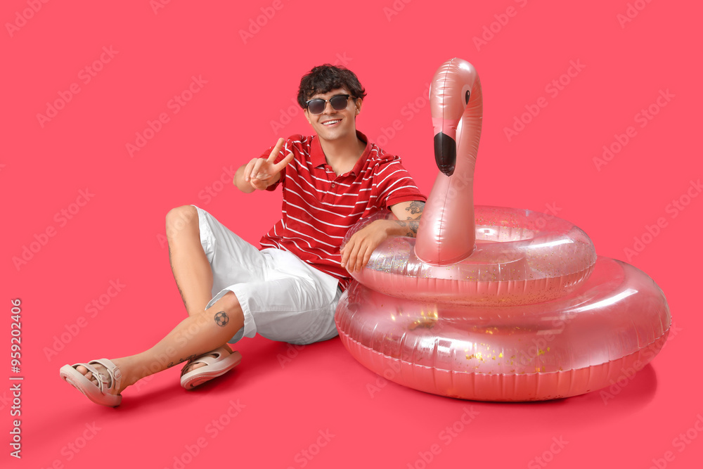 Wall mural Young man with swim rings showing victory gesture on red background