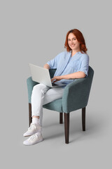 Young woman using laptop in soft armchair on light background