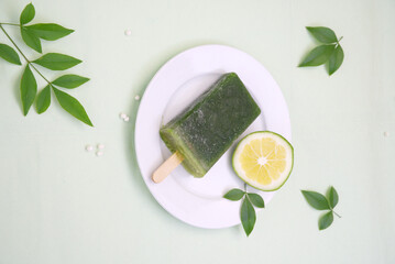 Close-up of green ice cream on white plate, green lemon, green leaves, top view