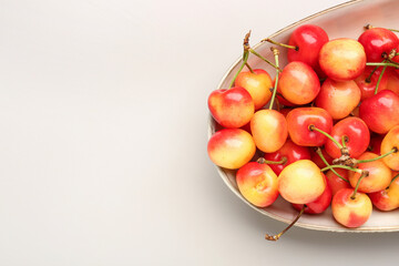 Bowl with sweet yellow cherries on grey background