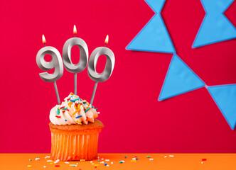 Birthday cupcake with candle number 900 on a red background with blue pennants