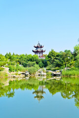 A pavilion reflected on lake with green trees, long shot of a corner of park