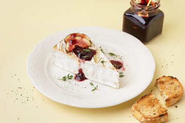 Plate with tasty baked Camembert cheese on yellow background