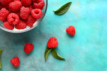 Glass bowl with fresh raspberries and mint on blue background