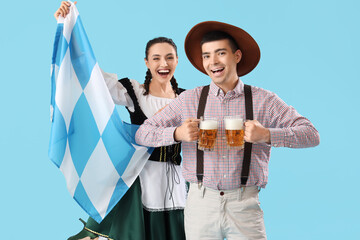 Young couple in traditional German clothes with beer and Bavarian flag on blue background