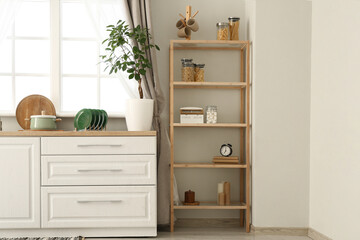 Interior of stylish kitchen with white counters, window, houseplant and shelving unit