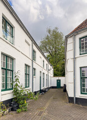 Brugge, Flanders, Belgium - June 22, 2024: White facades at dead-end alley of historic residential houses of Wevershof with plants and tree foliage