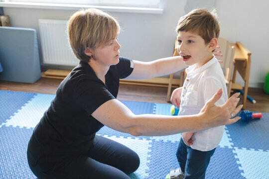 Beautiful physical therapist assists a young boy with movement disorders as he practices standing in a nurturing therapy environment
