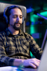 Male individual wearing wireless headphones while browsing the internet on his digital laptop. Closeup of man using portable computer and listening to podcasts on audio headset.