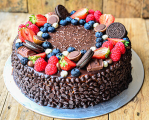 A chocolate cake with strawberries, blueberries, and oatmeal cookies on top. The cake is decorated with chocolate chips and has a rustic, homemade feel