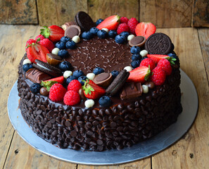 A chocolate cake with strawberries, blueberries, and oatmeal cookies on top. The cake is decorated with chocolate chips and has a rustic, homemade feel