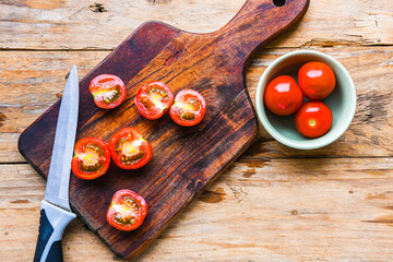 A wooden cutting board with a knife on it and a bowl of tomatoes