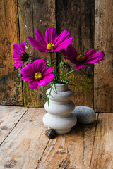 A vase with purple flowers sits on a wooden table beside a rock. The flowers are arranged in a way that they are all facing the same direction, creating a sense of harmony and balance