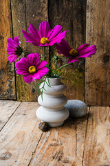 A vase with purple flowers sits on a wooden table beside a rock. The flowers are arranged in a way that they are all facing the same direction, creating a sense of harmony and balance